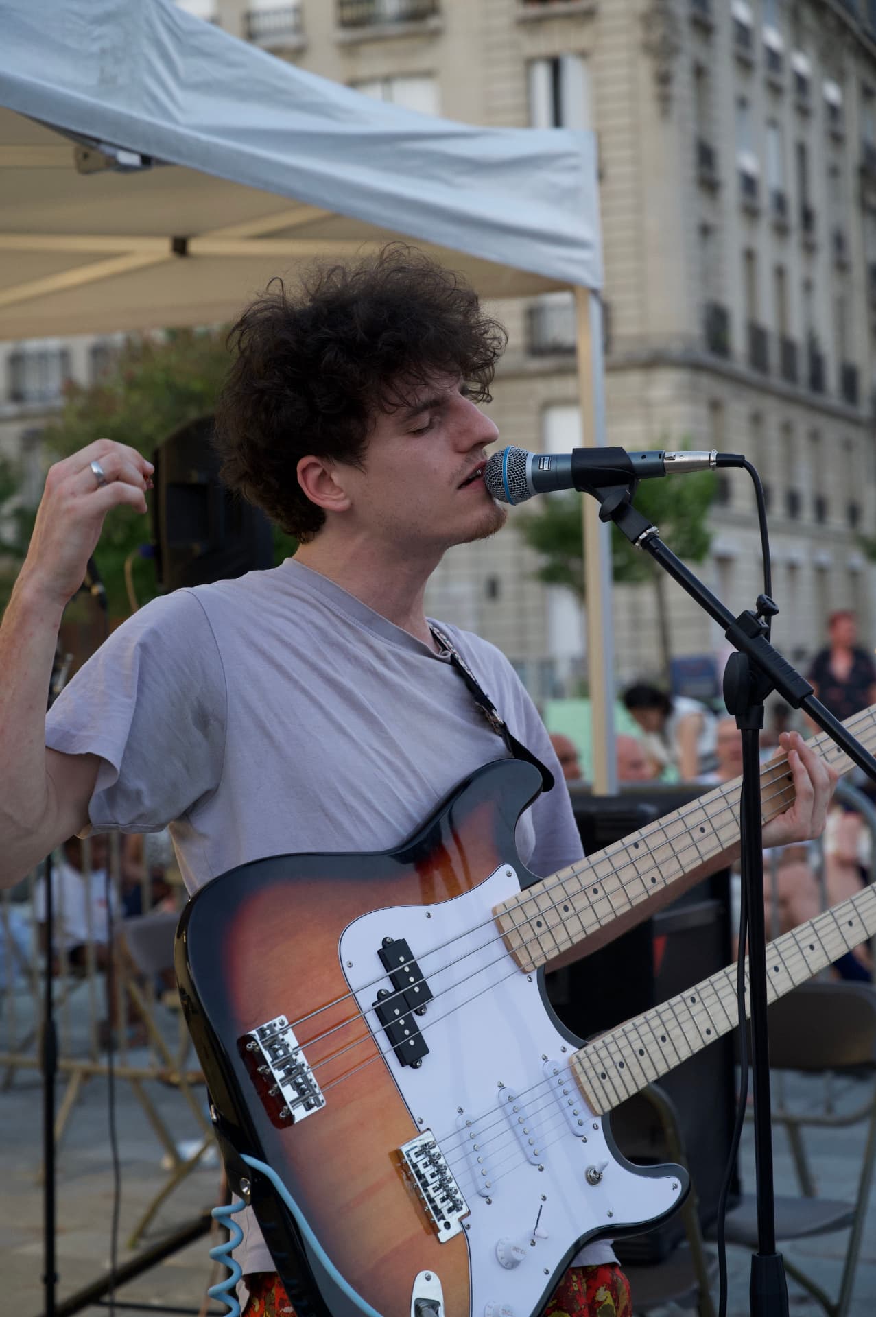 Un musicien chante et joue d'une guitare double manche, en extérieur.