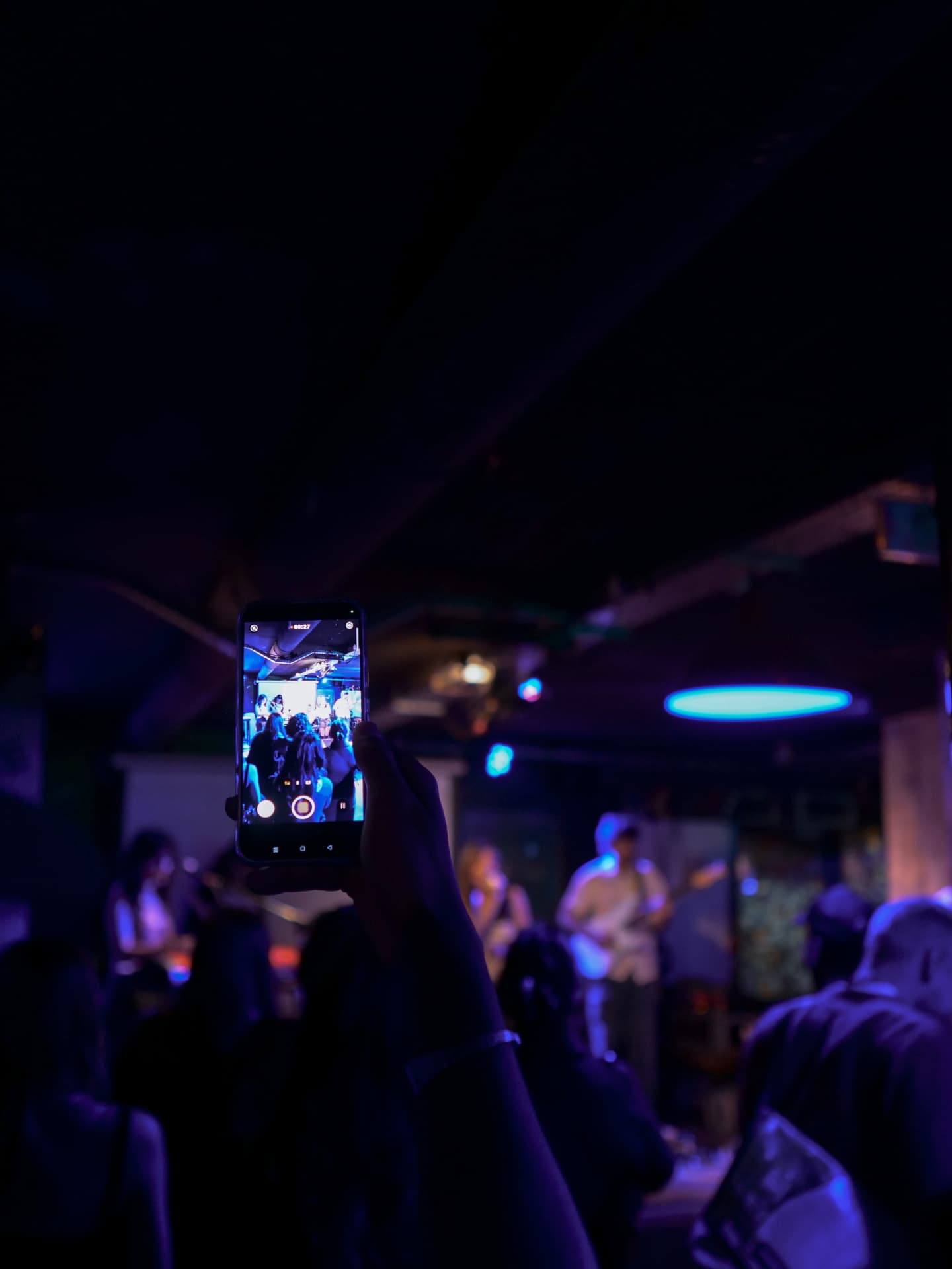 Le public filme un concert depuis l'audience, téléphone levé.
