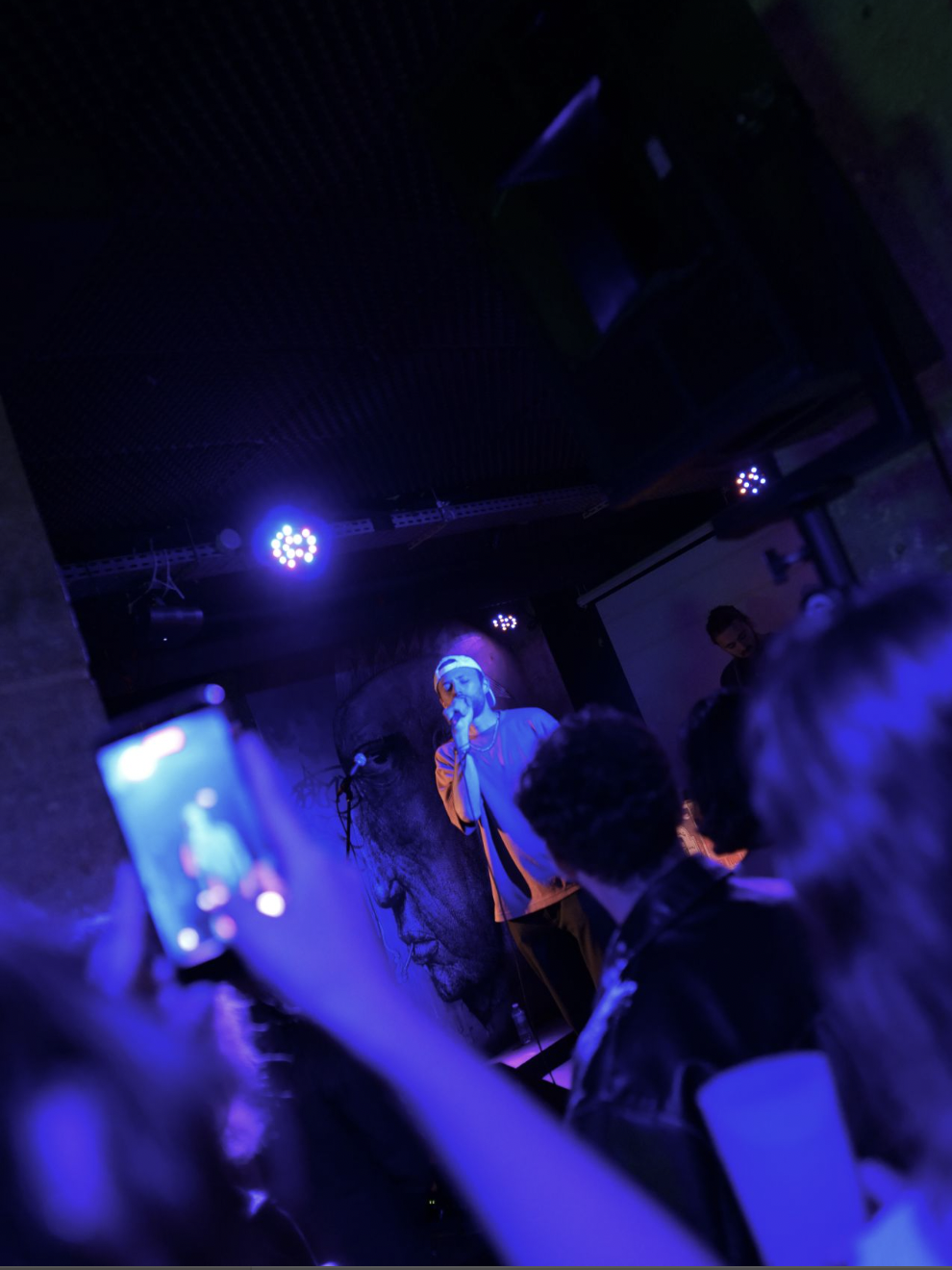 Un chanteur sur scène sous un projecteur bleu, dans un club.